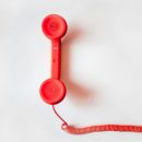 Vintage red phone handset with coiled cable on a clean white background, classic communication device.
